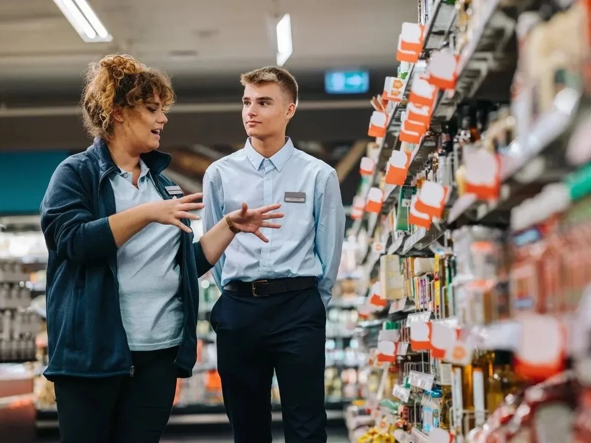 Two retail staff in uniform talking on a supermarket shop floor