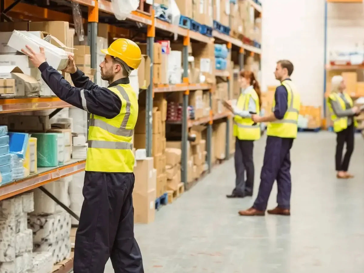 Warehouse crew in hi-vis vests and black workwear among storage racks